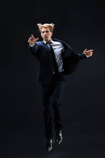 istock In a dark studio, a man in a sharp navy suit leaps mid-air, 2202107988
