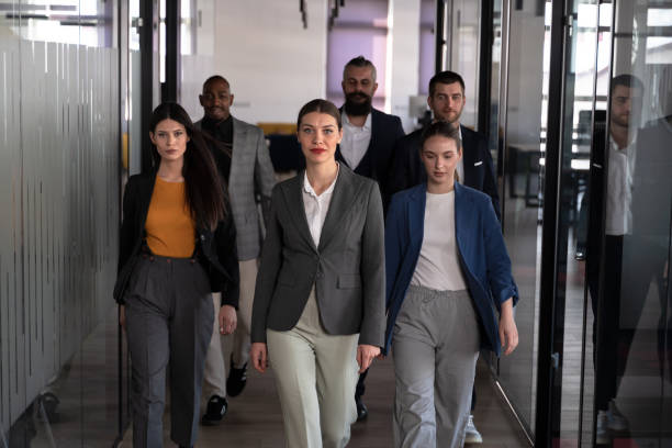 istock Confident business professionals walking through a modern office hallway, led by a determined woman in a suit. Concept of leadership, teamwork, corporate success, and professional ambition 2202109094