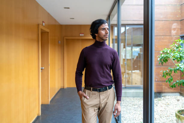 istock Businessman walks thoughtfully down a modern office corridor, looking out the window at the courtyard 2202110744