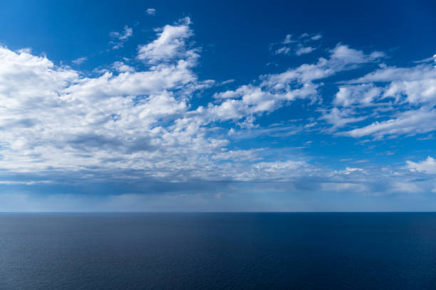 The vast ocean stretches out to the horizon under a serene sky filled with soft, fluffy clouds, creating a sense of peace and tranquility.