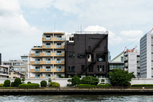 Residential buildings line the riverbank under a cloudy sky, showing diverse architectural styles in an urban setting.