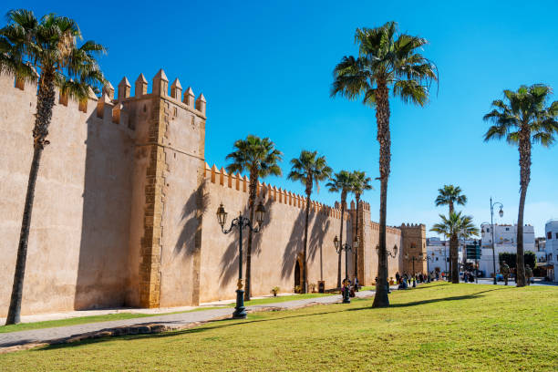 Explore the towering walls of the Kasbah of the Udayas, punctuated with palm trees against a blue sky, showcasing Moroccan architecture in Rabat.
