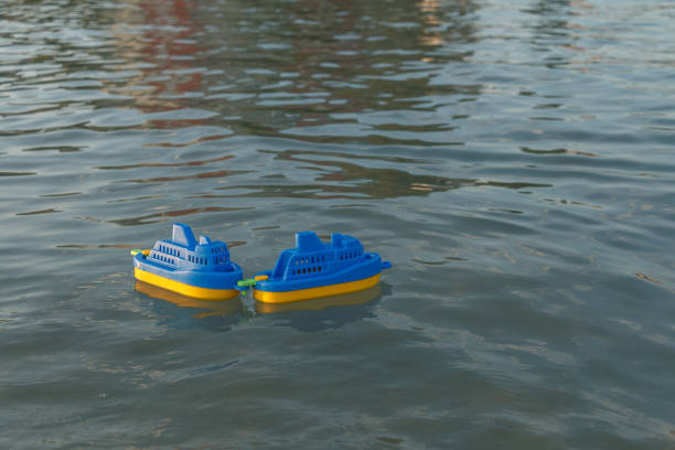 Two blue and yellow plastic toy boats float on a calm water surface. Gentle ripples reflect the sunlight, creating a peaceful and playful scene.