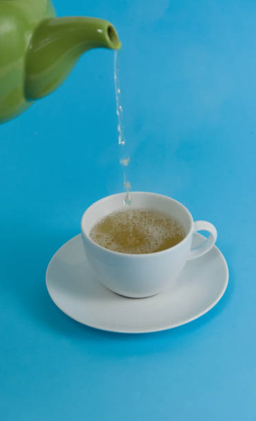 istock Green teapot pouring tea into a white cup 2202124738