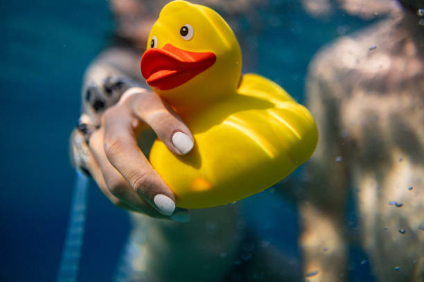 A cheerful yellow rubber duck and its smaller companion float peacefully in a clear blue pool, radiating a joyful summer vibe under the sun.