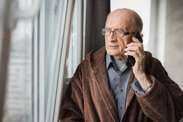 istock Elderly man looking through the window and having phone conversation 2202133897