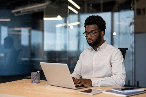 istock Serious thinking man working inside office with laptop, businessman in shirt typing on computer keyboard, working in evening at work 2202134330