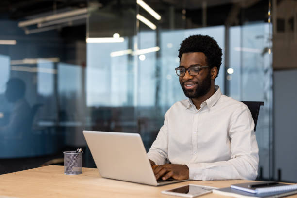 istock Young successful businessman working on laptop inside office, man in light shirt smiling contentedly, typing on laptop keyboard at workplace 2202134335