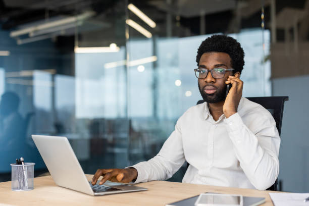 istock Portrait of serious confident businessman, man thoughtfully looking at camera, working inside office at workplace with laptop, talking on phone 2202135780