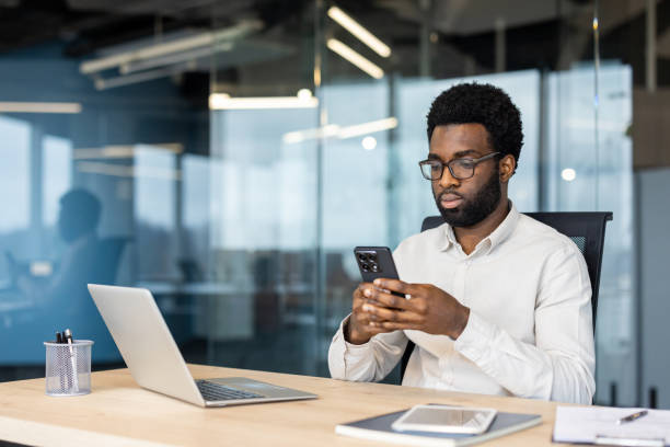 istock Serious focused man using app on phone. Businessman thinking sitting at desk in middle of office, typing text message on smartphone, and browsing online internet pages 2202135784