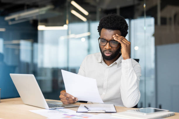istock Tired and overworked man with paperwork inside office. Office worker dissatisfied with financial report. Businessman holding document, tax statistical form in hands 2202135796