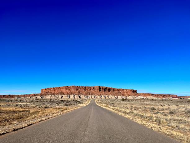 Route 66 stretches through the desert in New Mexico towards a Mesa under a vibrant blue sky, offering a picturesque view of the iconic American highway