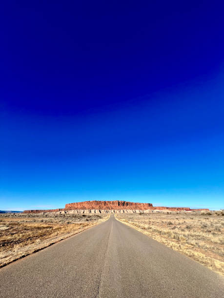 Scenic view of a long straight road leading towards a mesa in the distance, under a vibrant blue sky in New Mexico, showcasing the iconic Route 66