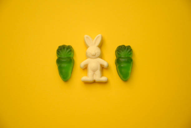 istock Easter gummy rabbits and candy carrots on vibrant yellow background 2202136242