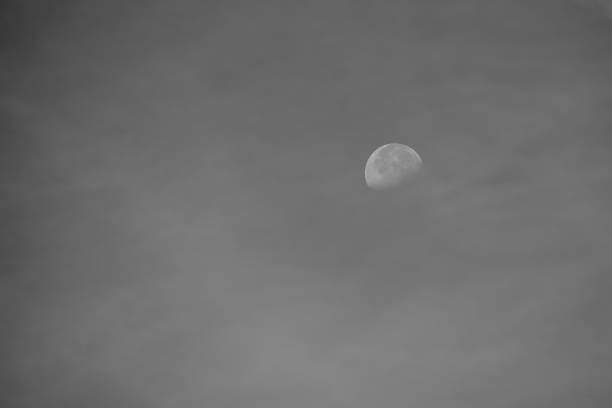Moon seen during the day against a blue sky on black and white