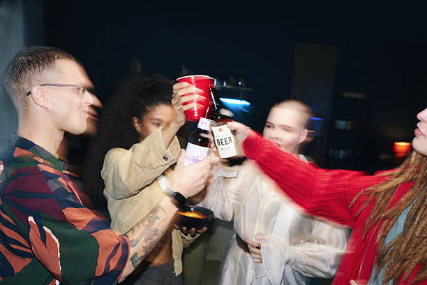 Group of diverse friends enjoying party, raising their drinks in lively atmosphere. Elements include various beverages, casual attire, and festive environment