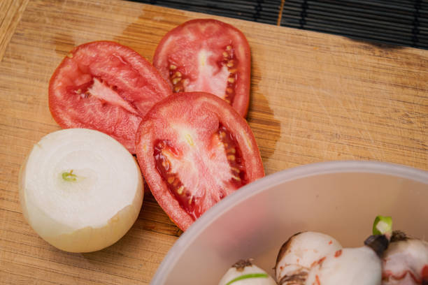 Preparation of a vegetable salad with fresh tomatoes, pepper, garlic and onions. Chopped garlic on a wooden cutting board and fresh vegetables on a dark background