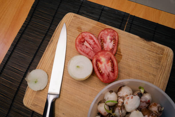 Preparation of a vegetable salad with fresh tomatoes, pepper, garlic and onions. Chopped garlic on a wooden cutting board and fresh vegetables on a dark background