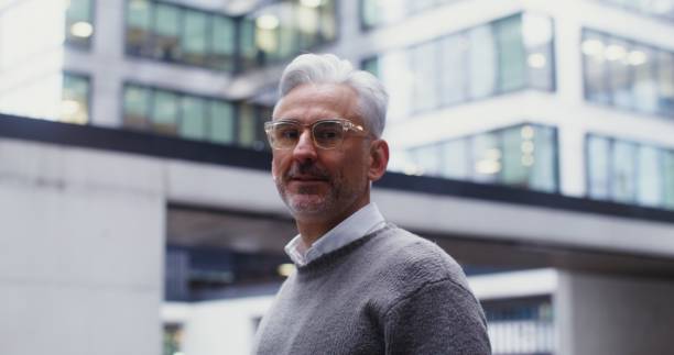 istock A gray-haired man smiles looking at the camera while standing in business center 2202142577