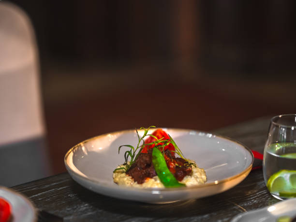 Delicately roasted meat pieces are neatly arranged on a white plate, accompanied by lime and radish slices, topped with sesame seeds. The use of chopsticks to pick up the dish highlights its color and unique flavors