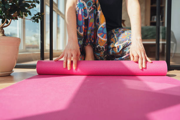 istock Practicing yoga, rolling a pink yoga mat indoors. 2202147504
