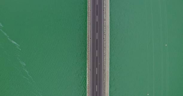 View from above, a narrow road bridge without cars, over a river with small ripples of waves. Video recording from a drone