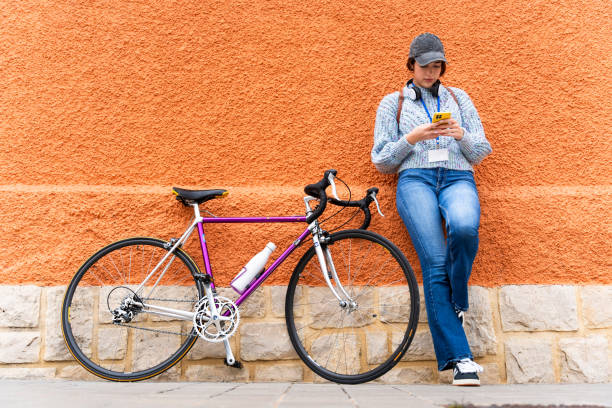 istock Young woman using smartphone leaning on orange wall with her racing bicycle 2202149753