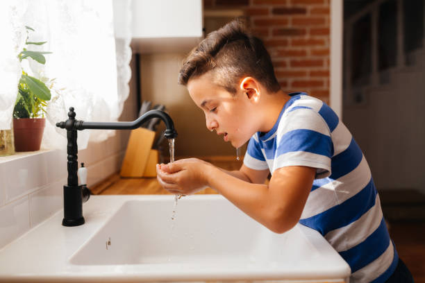 istock Boy Washing His Face with Fresh Water in a Cozy Kitchen 2202152450