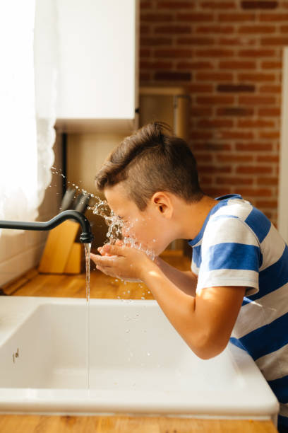 istock Boy Washing His Face with Fresh Water in a Cozy Kitchen 2202152534