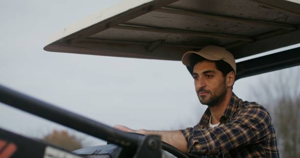 istock Young farmer rides a tractor looking around, inspecting his property 2202156064