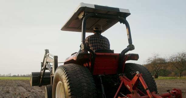 A young European-looking farmer turns a tractor around and begins to drive along a new row, plowing a field on an autumn day and turns around, checking the quality of work