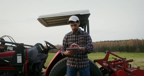 istock Young tractor driver uses a tablet leaning on a modern agricultural tractor 2202156806