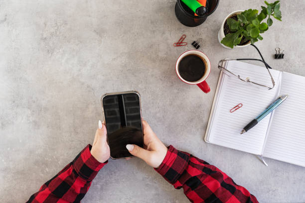Top view of a woman's hand holding a smartphone over her modern office desk