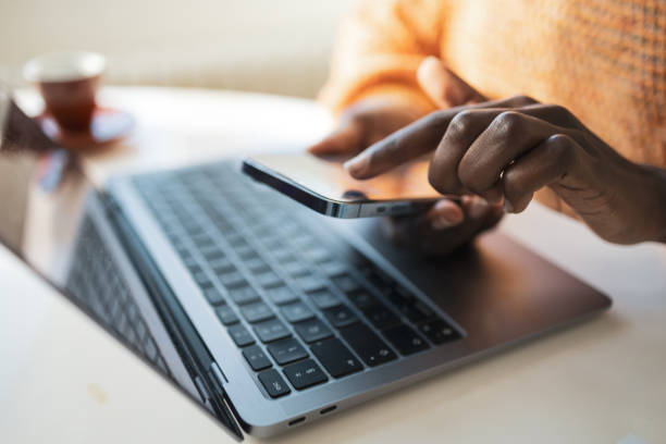 istock Crop black female freelancer using smartphone with laptop in home office 2202157998