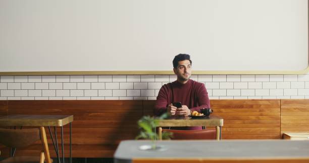 istock A young man sits in a cafe and uses phone, from time to time looking around 2202158885