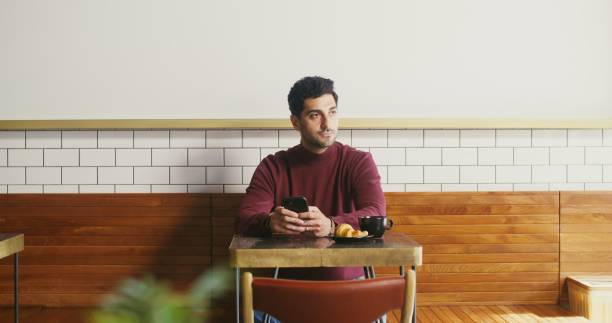 A young man sits in a cafe and uses phone, from time to time looking around