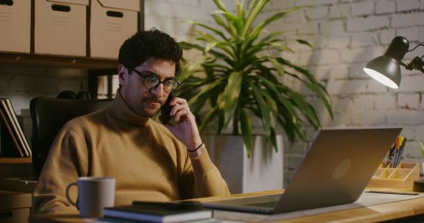istock Young man talking on a mobile phone and using a laptop in office 2202159706
