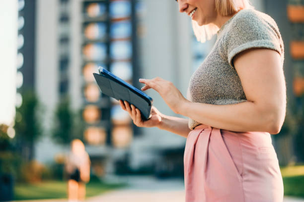 istock Smiling Woman Using a Tablet in a Modern Urban Setting Outdoors 2202159808
