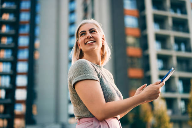 istock Confident Woman Smiling Outdoors Using a Smartphone in Urban Setting 2202159812