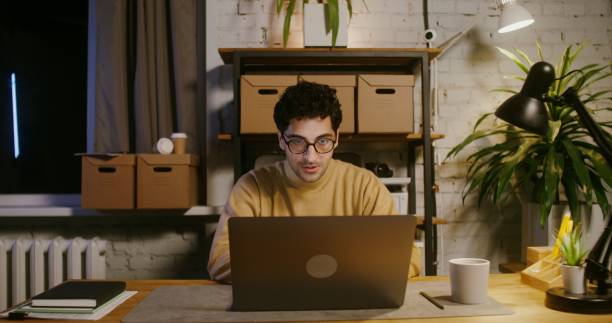 istock Dollar bills start to fall from the ceiling, delight a man working at a laptop 2202160531