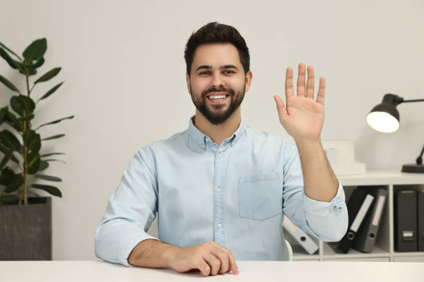 istock Happy young man waving hello during video chat indoors, view from web camera 2202160832
