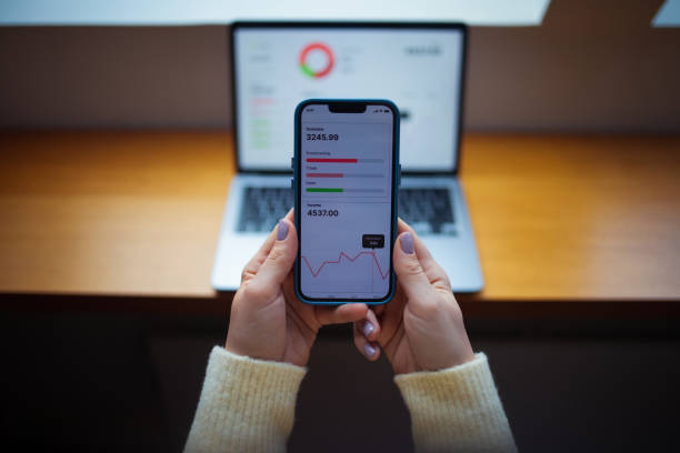 istock Person Analyzing Financial Data on a Smartphone With Laptop in Background 2202165985