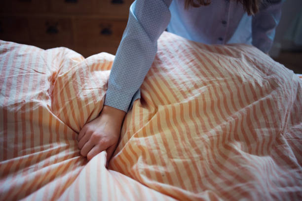 Close-up of a personâs hand smoothing a beige and orange striped duvet, emphasizing care and organization in a cozy, intimate home setting. The scene evokes neatness, comfort, and attention to detail.