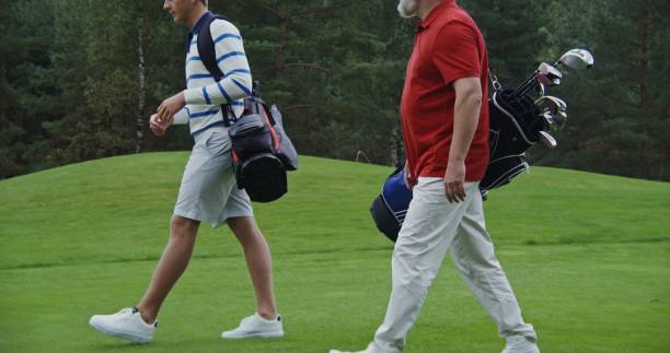 istock Two men walk along the golf course with game equipment chatting with each other 2202166120