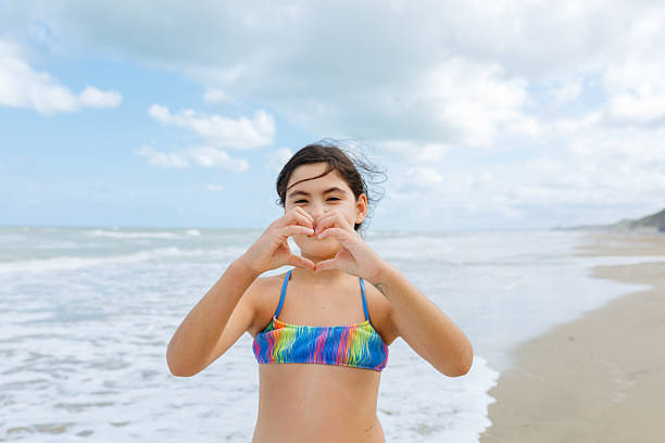 smiling dark-haired girl showing heart hands standing on the beach