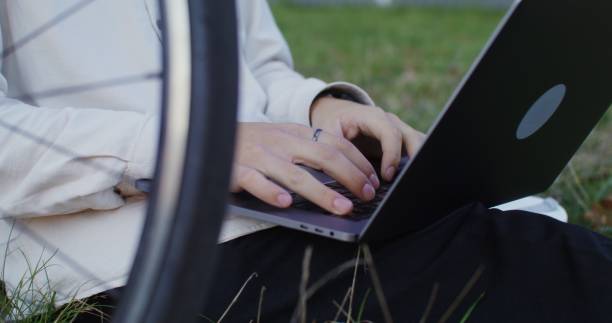 istock A young man uses a laptop sitting on the grass under a tree outdoors. 2202166659