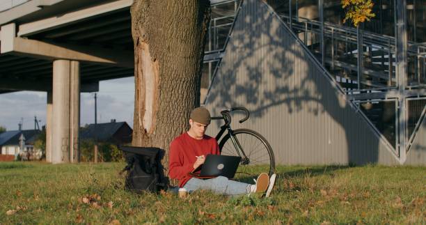 istock A man uses a graphics tablet and a laptop, sitting on the ground under a tree 2202166754