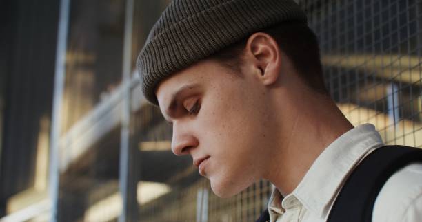 A young man of European appearance in a knitted hat uses a mobile phone and drinks coffee, close-up