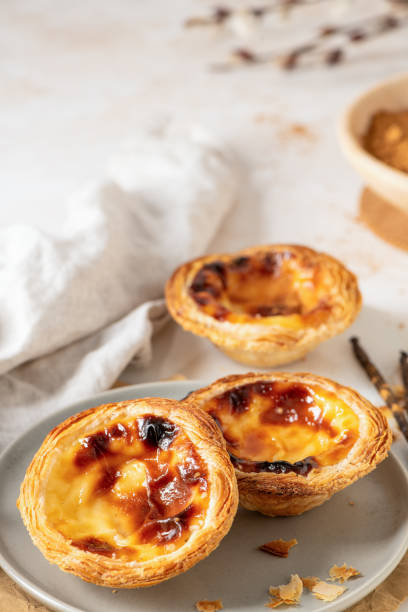 istock Three Pastel de Nata, Portuguese custard tarts, are presented on a plate with cinnamon and vanilla beans. 2202171052