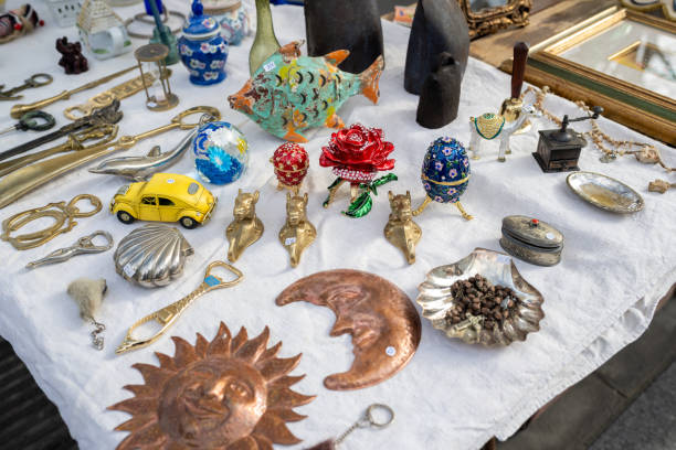 A collection of antique objects and trinkets, including brass keys, figurines, and decorative items, displayed on a white cloth at a flea market. The vibrant and eclectic assortment reflects vintage charm and craftsmanship.